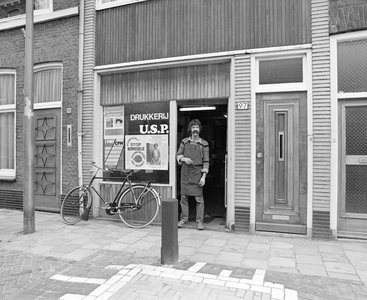 882335 Gezicht op de winkelpui van drukkerij U.S.P. (Kapelstraat 97) te Utrecht, met de drukker in de deuropening.